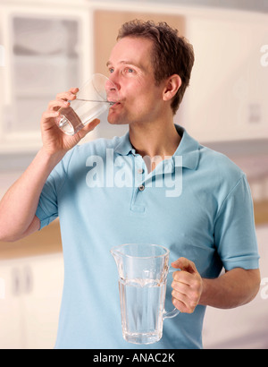 MAN IN KITCHEN DRINKING GLASS OF WATER Stock Photo