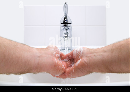 Man washing his hands with soap under running water in a white hand basin Stock Photo