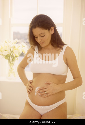 Heavily pregnant woman applying moisturising cream to her tummy to help prevent stretch marks, U.K. UK Stock Photo