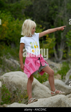 Small blonde girl in a white and pink top points into the distance Stock Photo