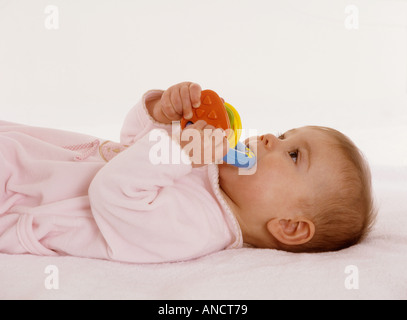 Baby girl lying on her back chewing on a plastic teething ring Stock Photo