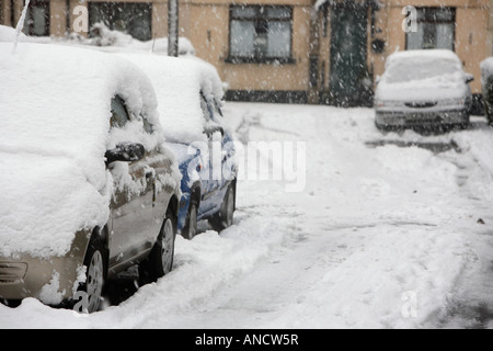 cars parked abandoned covered in snow in side street with car tyre tracks Stock Photo