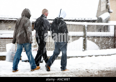 three young men walking along footpath in snowstorm Stock Photo