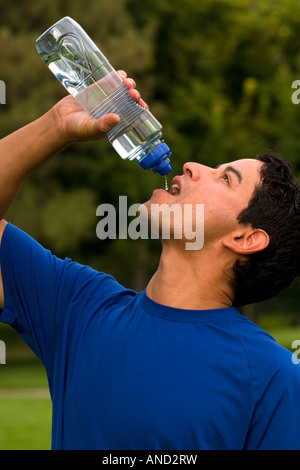 Young man drinks from water bottle after a run in the park Stock Photo