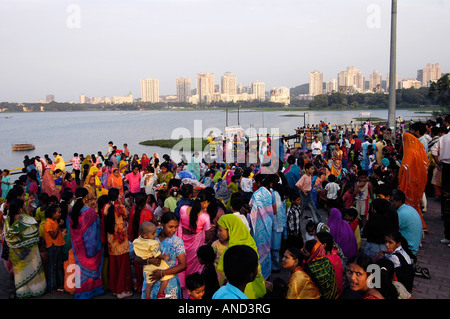 Crowd of Indian women and children attending a Hindu festival near a lake in Mumbai, with skyscrapers visible in background. Stock Photo