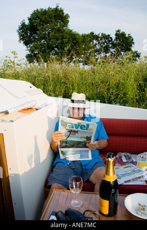Holidaymaker reads Travel section of broadsheet newspaper on river cruiser Norfolk Broads UK Stock Photo