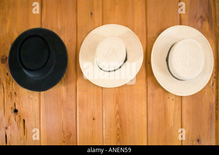 Three hats, two white, and one black, hanging on hooks on the wall. Stock Photo