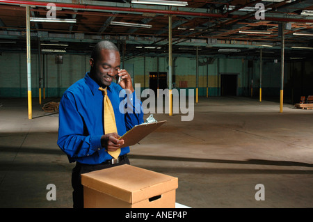 Black businessman standing in empty factory warehouse speaking on a mobile cell phone Stock Photo