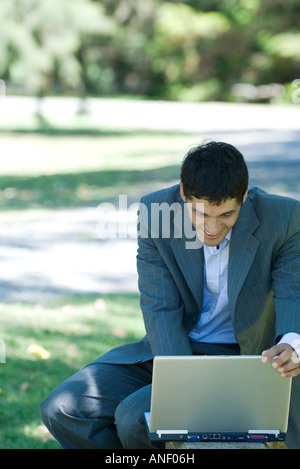 Businessman using laptop outdoors, adjusting screen and smiling Stock Photo