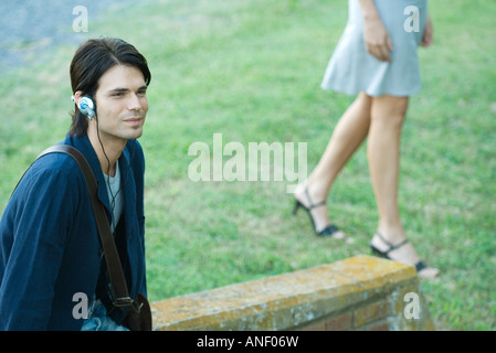Man sitting in park,  listening to headphones while woman walks by Stock Photo