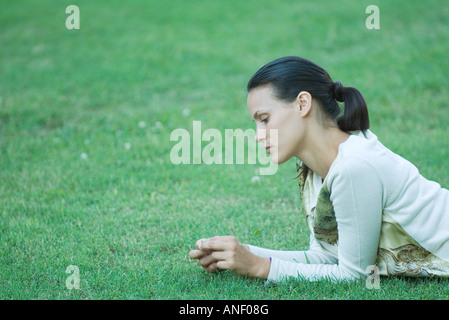 Young woman lying on grass, holding blade of grass in fingers Stock Photo