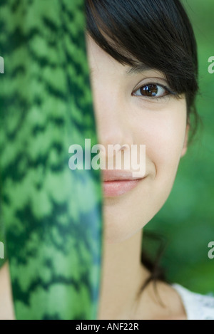 Woman holding up snake plant leaf in front of half of face, portrait Stock Photo
