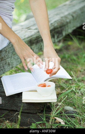 Woman reading book and eating cherry tomatoes, cropped Stock Photo