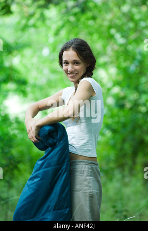 Young camper rolling up sleeping bag, smiling at camera