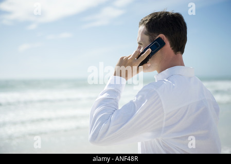 Young man using cell phone on beach, side view Stock Photo