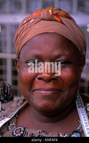 Smiling middle aged African Street tailor woman in traditional colourful clothing & hat Jinja City Uganda East Africa Stock Photo