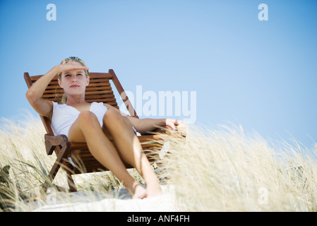 Young woman sitting in deckchair on beach, shading eyes Stock Photo