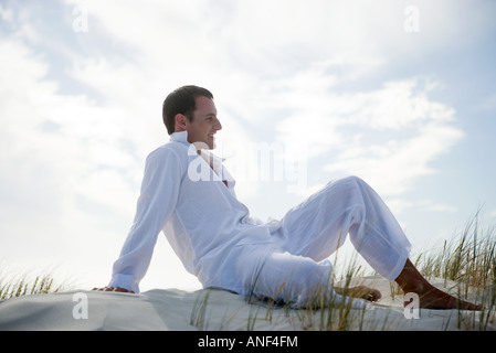 Young man lounging on dune, side view Stock Photo