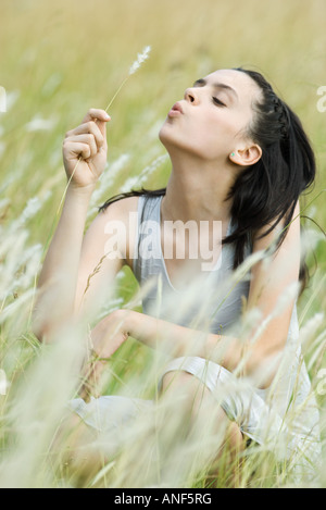 Teen girl sitting in field, holding sprig of long grass Stock Photo