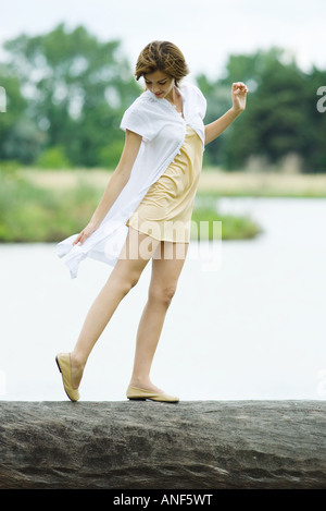 Young woman walking along log, looking down at foot, full length Stock Photo