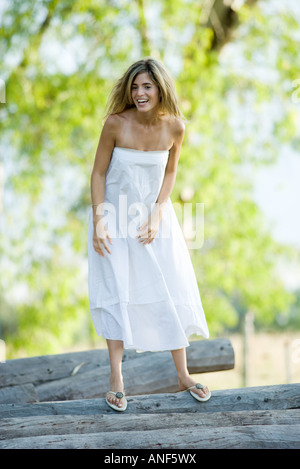 Young woman in dress standing on pile of logs, laughing, full length Stock Photo