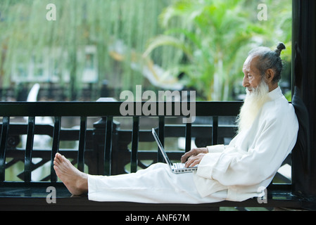 Elderly man in traditional Chinese clothing, barefoot, using laptop Stock Photo