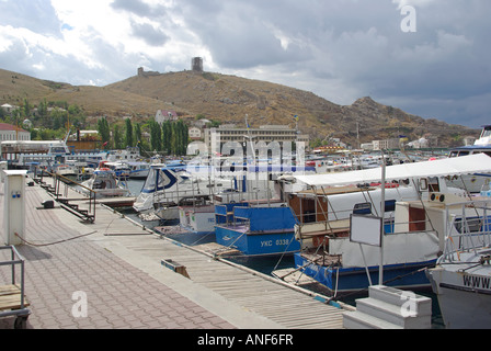 Balaclava bay harbour one time soviet nuclear submarine base motor boats beside promenade hillside and Genoese fort beyond Stock Photo