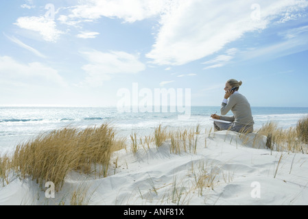 Woman sitting on dunes at beach, using cell phone Stock Photo