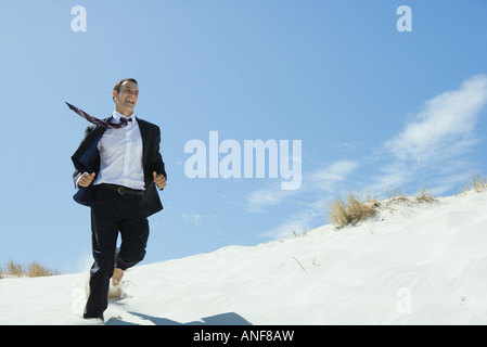 Businessman running across sand dune, low angle view Stock Photo