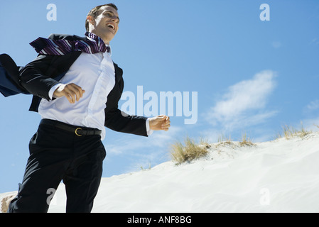 Businessman running across sand dune, low angle view Stock Photo