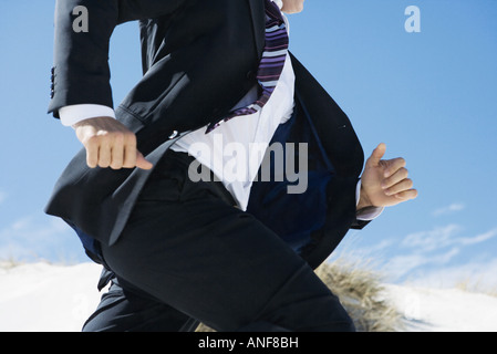 Businessman running, sand dune in background, cropped view of mid section Stock Photo