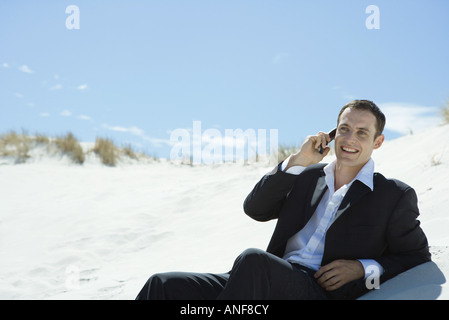 Businessman sitting on sand dune, using cell phone Stock Photo