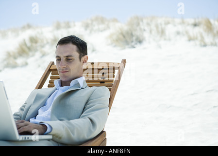 Businessman sitting in deck chair at beach, using laptop Stock Photo
