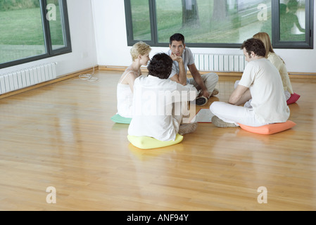 Group therapy session, adults sitting in circle on floor, talking Stock Photo