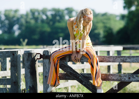 Young woman sitting on top of rural fence, looking down Stock Photo