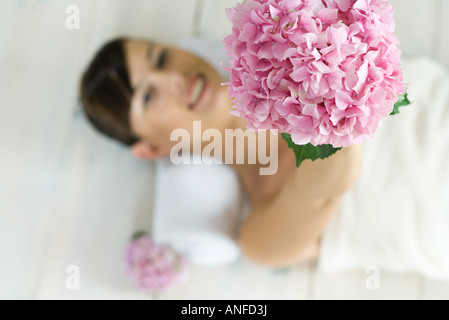 Young woman lying on back, holding up flower, view from directly above Stock Photo