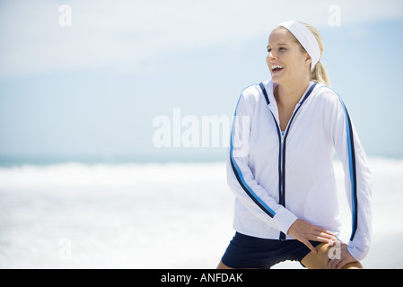 Young woman in active wear on beach, stretching and laughing Stock Photo
