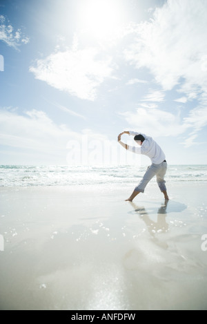 Young man standing in surf, stretching, rear view Stock Photo