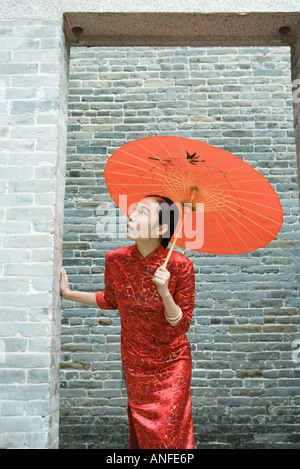 Young woman wearing traditional Chinese clothing, holding parasol, looking up through doorway Stock Photo