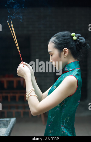 Young woman wearing traditional Chinese clothing, holding up incense, side view Stock Photo