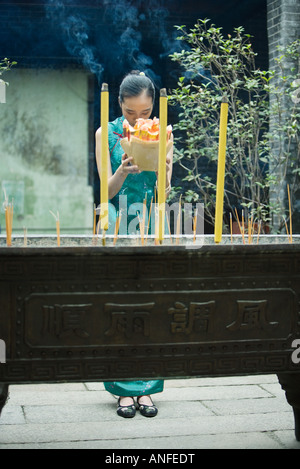 Young woman standing in temple courtyard, holding up religious offering, eyes closed and head bowed Stock Photo