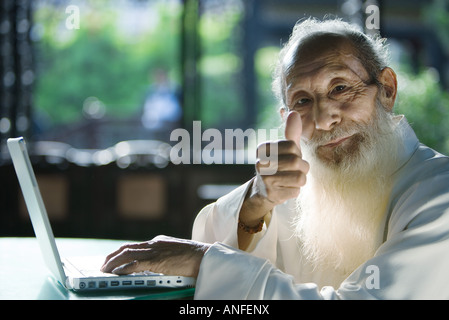 Elderly man wearing traditional Chinese clothing, using laptop, giving thumbs up to camera Stock Photo