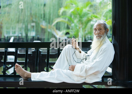 Elderly man wearing traditional Chinese clothing, listening to MP3 player, full length Stock Photo