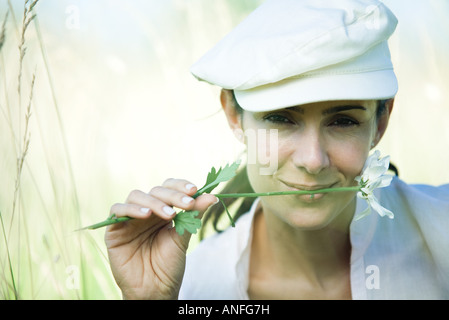 Woman in field, holding flower between lips Stock Photo