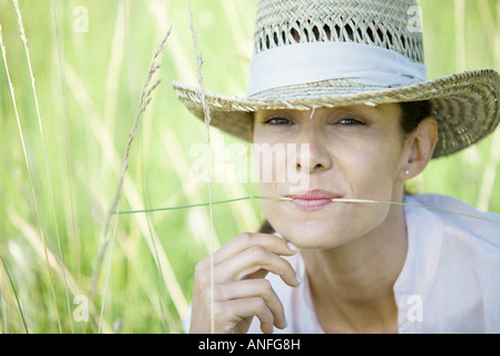 Woman in field, blade of grass between lips, looking at camera Stock Photo