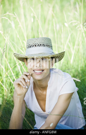 Woman in field, blade of grass between lips, looking at camera Stock Photo