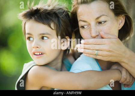 Mother and son, woman holding boy on back, whispering to him Stock Photo