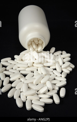 Plain white bottle on it's side with large pool of white oval tablets or caplets before it. Stock Photo