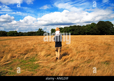 Father carrying child on shoulders across sunny field Stock Photo