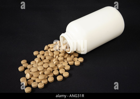 Plain white bottle on it's side spilling thick round mottled brown tablets in large pool before it Stock Photo